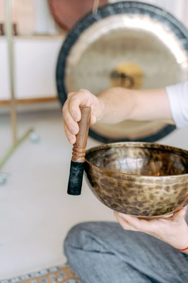 Persona fent sonar un bol tibetà amb una maça de fusta durant una sessió de bany de so.