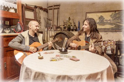 Els dos músics al voltant d'una taula amb un porró de vi i una baralla de cartes..