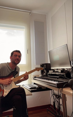 El músic Gil Grau assegut agafant una guitarra. Darrera seu, un teclat.