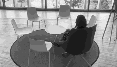 Imatge promocional de la Biblioteca Humana de Vic. Una noia d'esquena asseguda en un cercle de cadires buides..